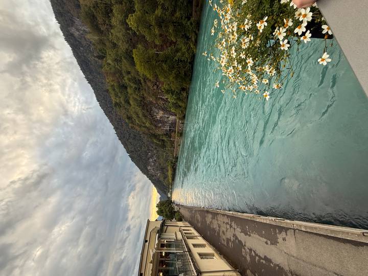 Turquoise river flowing between forested hills under cloudy sky.