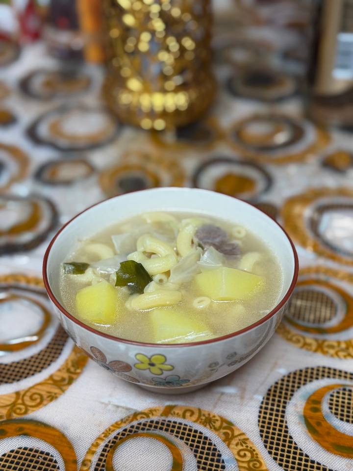 Bowl of traditional Mongolian noodle soup with potatoes and greens on patterned table.