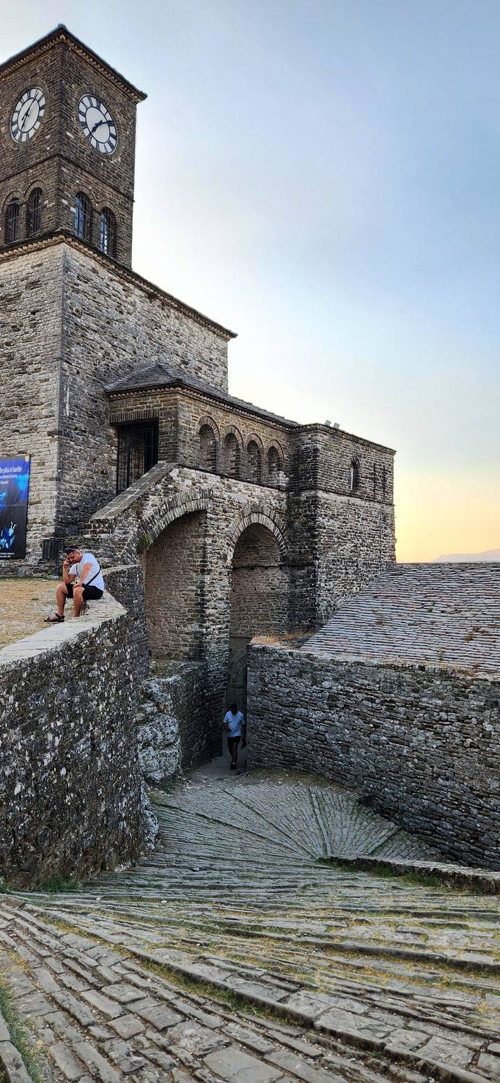 Stone fortress walls and arches at sunset with a lone visitor sitting on the ledge.