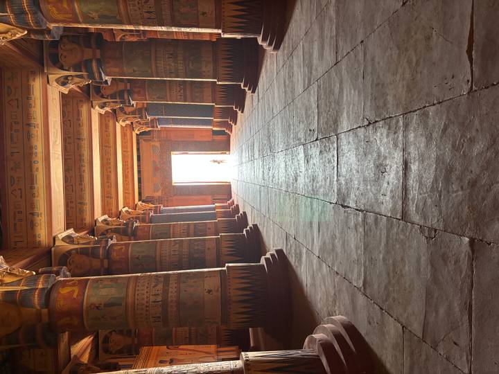 Grand hypostyle hall with vividly painted ancient-Egyptian columns leading toward a bright doorway.