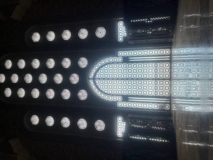 Majestic patterned glass window wall inside Hassan II Mosque casting reflective light on the polished floor.