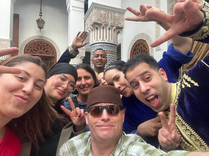 Cheerful group selfie with travelers and locals making peace signs in a traditional courtyard.