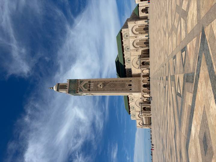 Wide view of the towering minaret and vast plaza of Hassan II Mosque under dramatic clouds.