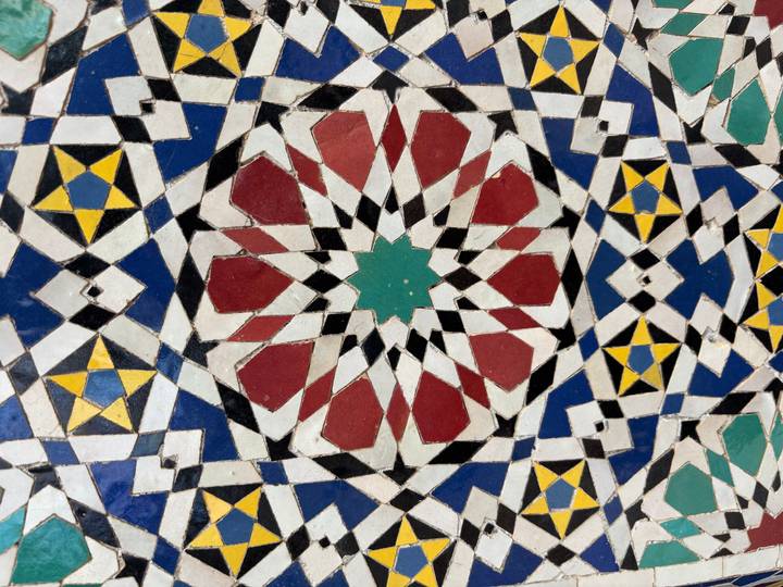 Close-up of colorful geometric zellij tile pattern with reds, blues, greens and yellows.
