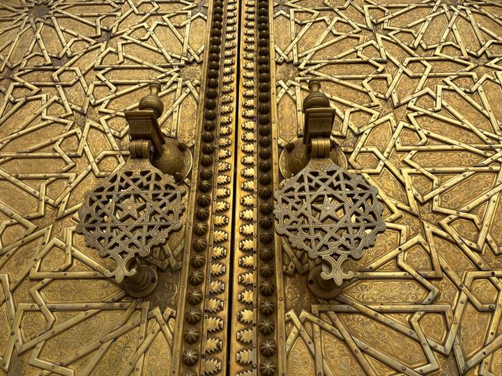 Ornate golden doors of a Moroccan palace with intricate metalwork knockers and geometric patterns.