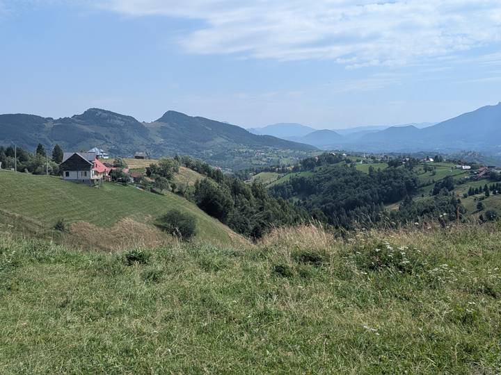 Expansive valley dotted with farmhouses and surrounded by rolling Carpathian peaks under clear skies.