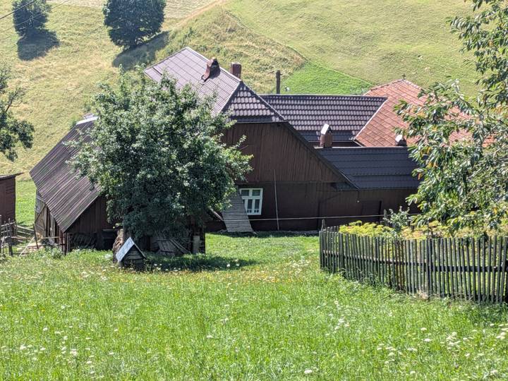 Traditional rural house with tin roof and surrounding garden fence beneath a sunny sky.