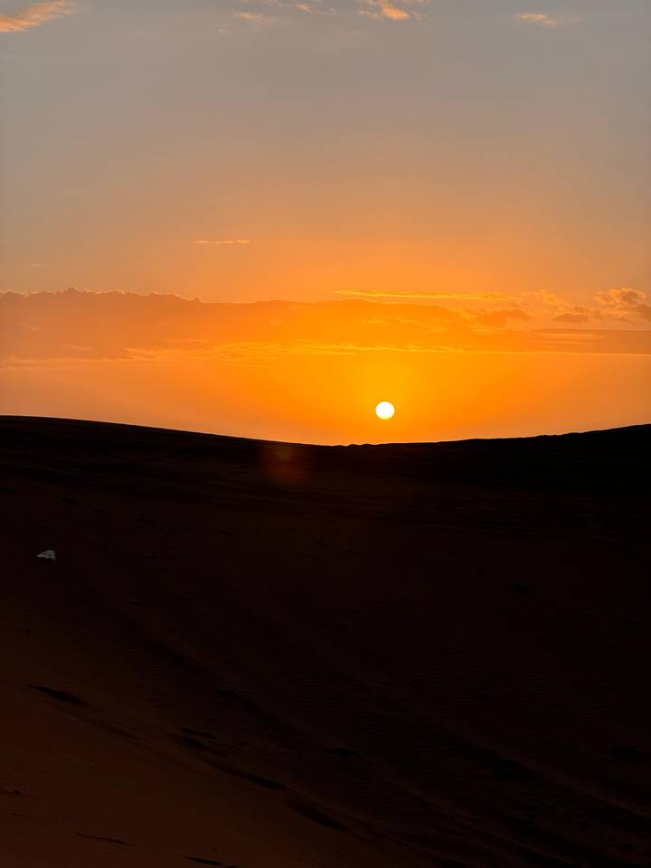 Brilliant orange sun setting over rolling sand dunes in the desert.