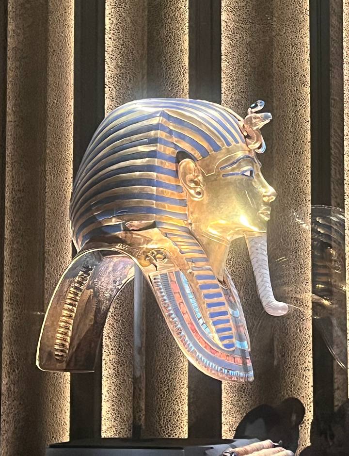 Close-up side profile of the gilded death mask of Tutankhamun displayed in a museum.