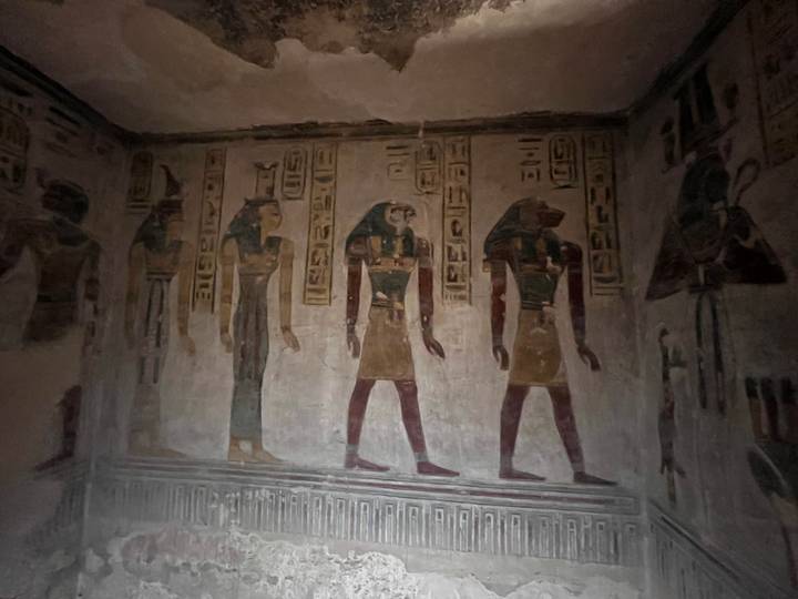 Dimly lit tomb wall covered with painted hieroglyphs and Egyptian deities in profile.
