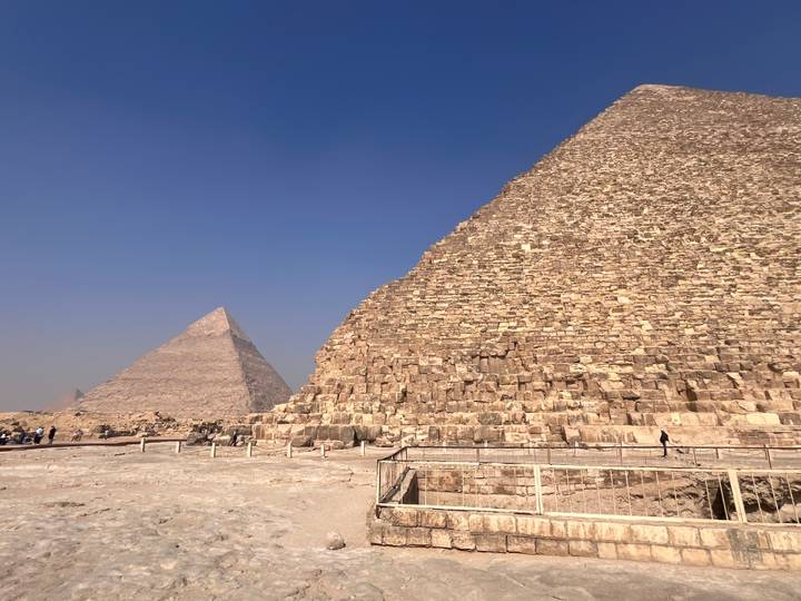 Wide shot of two massive pyramids at Giza with small groups of tourists exploring the base.