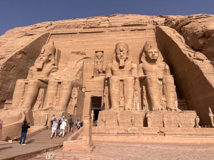Front view of the colossal statues of Ramses II at Abu Simbel with tourists gathered below.