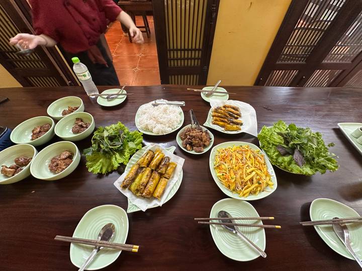Vietnamese family-style meal with spring rolls, pork, noodles and fresh herbs laid out on a wooden table