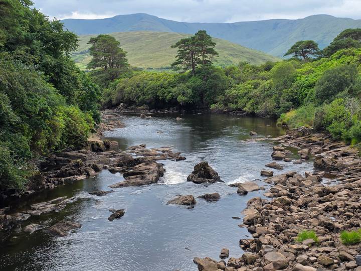 Serene river winding through rocky shallows with lush green hills in the distance.