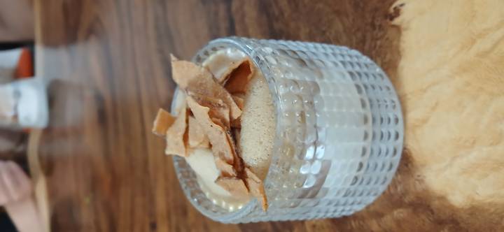 Small glass cup filled with creamy Vietnamese egg coffee topped with crisp flakes on a wooden table.