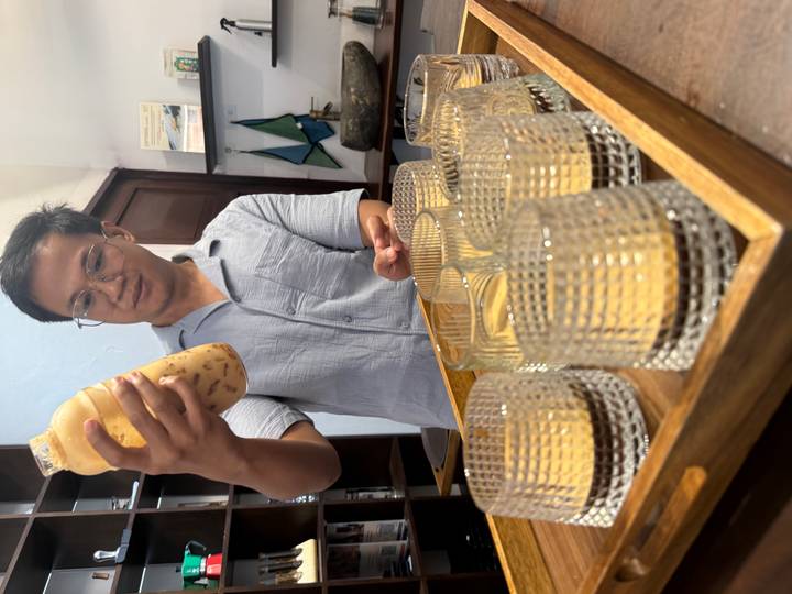 Young man holding a bottle of creamy coffee mixture over textured glasses on a wooden tray.