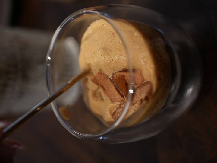 Close view of whipped egg coffee with chocolate flakes being stirred in a glass cup.