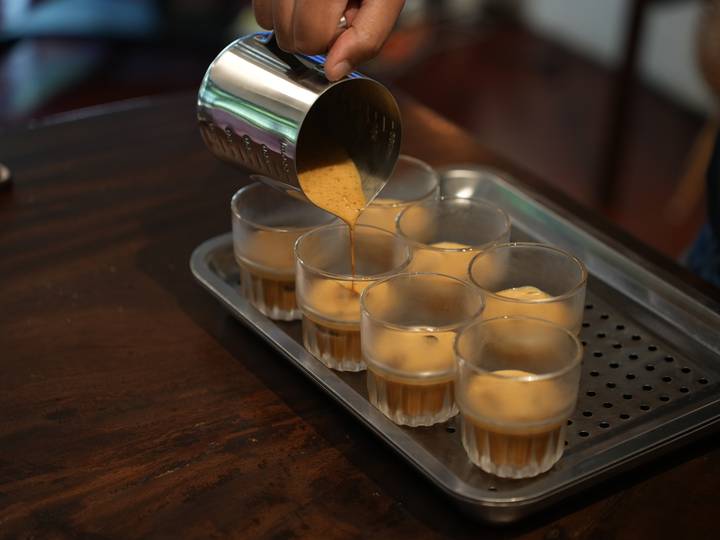Barista pours thick coffee into eight small glasses placed on a perforated tray.