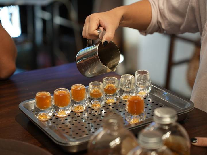 Stream of coffee poured into a neat row of tiny glasses giving off a warm hue.