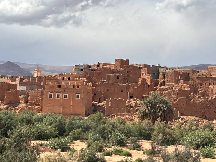 Panoramic view of the adobe ksar of Aït Benhaddou with palm groves in the foreground and arid hills beyond.