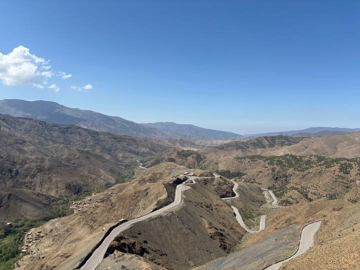 Sweeping view over winding mountain roads cutting through brown ridges of the High Atlas under a clear sky.