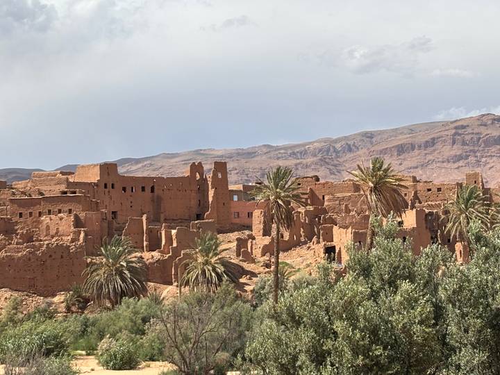 Ruined adobe village with scattered palm trees set against rugged desert hills.