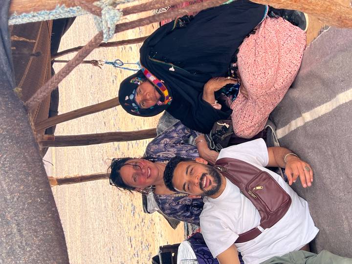 Travellers relax with a local woman inside a shaded nomad tent pitched on the desert floor.