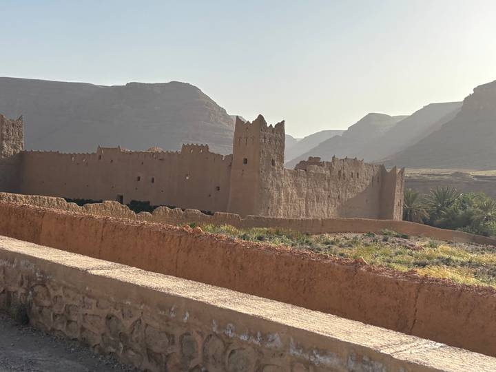 Fortified desert castle walls glow in soft evening light with layered mountains silhouetted behind.