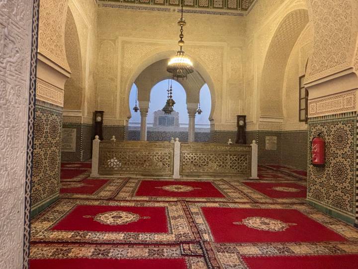 Intricately tiled and carpeted mausoleum interior with ornate arches and chandeliers.