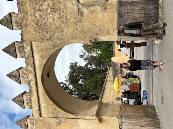 Traveller stands beneath a historic stone arch while locals pass through a busy Moroccan gateway.