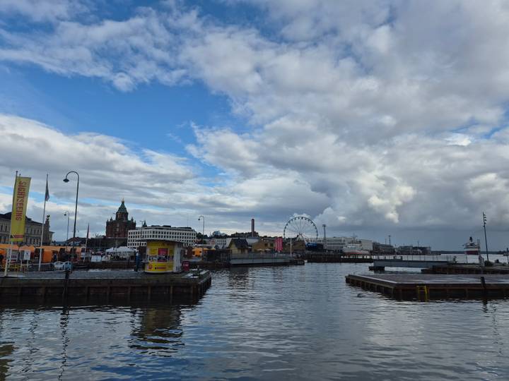 Helsinki harbourfront with Uspenski Cathedral, ferris wheel and boats beneath dramatic clouds.
