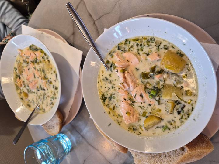 Two bowls of creamy salmon soup garnished with dill accompanied by bread on a marble table.