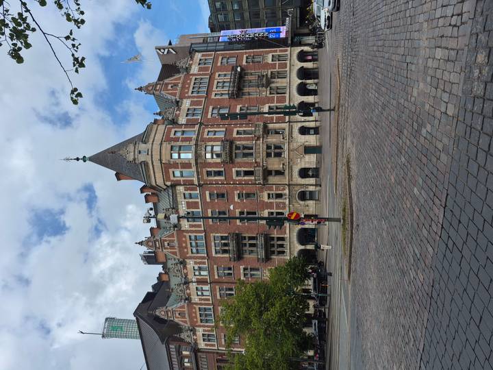 Grand red-brick historic building with ornate balconies and turrets facing a cobblestone street.