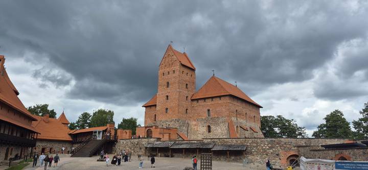 Red-brick Trakai Island Castle set against dramatic storm clouds with visitors exploring the courtyard.