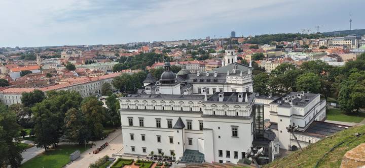 Elevated panorama of Vilnius Old Town with the white Presidential Palace complex in the foreground and terra-cotta rooftops beyond.