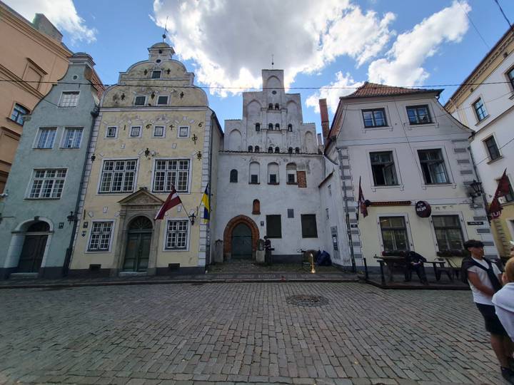 Historic Three Brothers houses in Riga’s Old Town, their pastel façades framed by cobblestone street and blue sky.