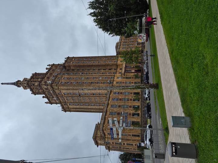 Tall Soviet-era Latvian Academy of Sciences tower rising above a grassy square on a gray day.