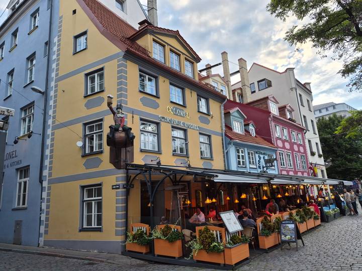 Colorful row of restaurants in Riga Old Town with outdoor diners beneath warm hanging lights.