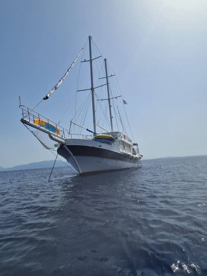 Anchored sailing yacht viewed low from water level on calm sea with hazy mountains in background.