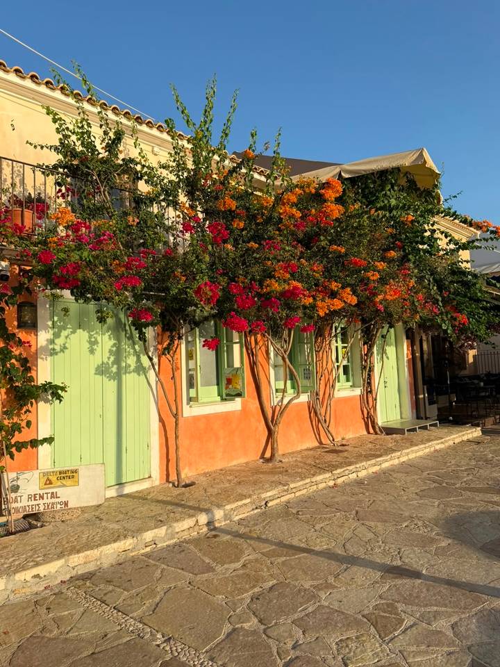Charming façade with mint-green shutters and vibrant orange and red bougainvillea blooming along street.