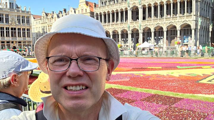 Traveler taking a selfie with Brussels’ Grand Place flower carpet and ornate guildhalls in the background.