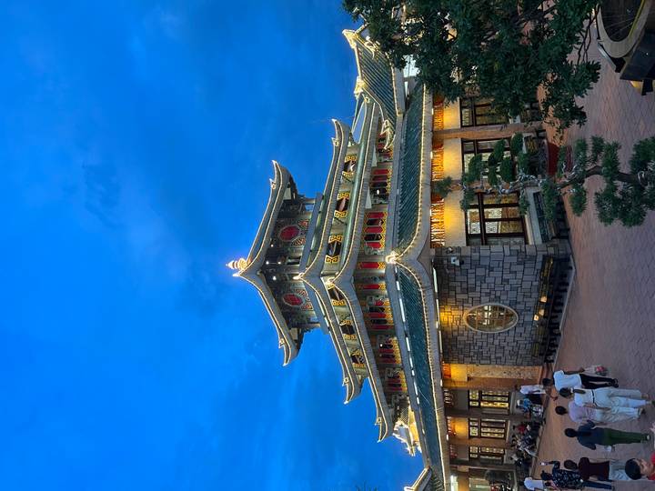 Illuminated multi-tiered pagoda glows against a deep blue evening sky as visitors stroll nearby.