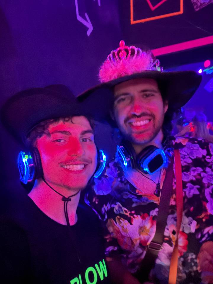 Low-light selfie of two men wearing glowing headphones at a silent disco.