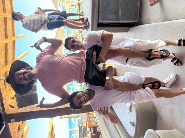 Two men lift a friend on their shoulders in an open-air bar by the sea.