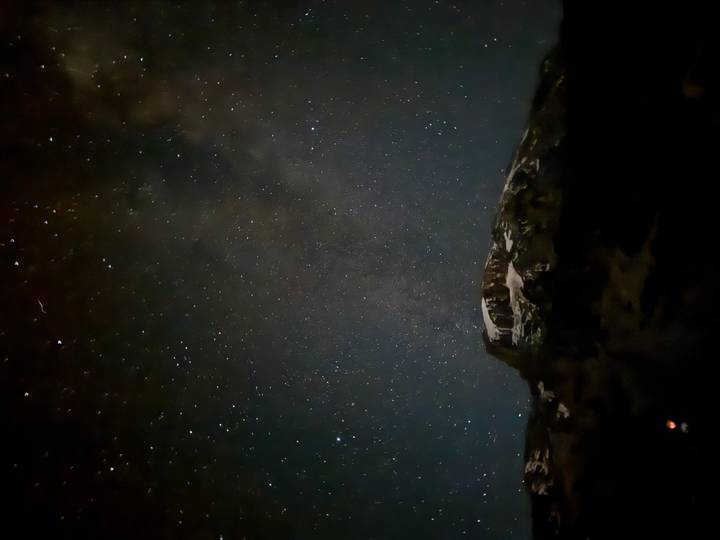Star-filled night sky over a snow-dusted mountain peak in near darkness.
