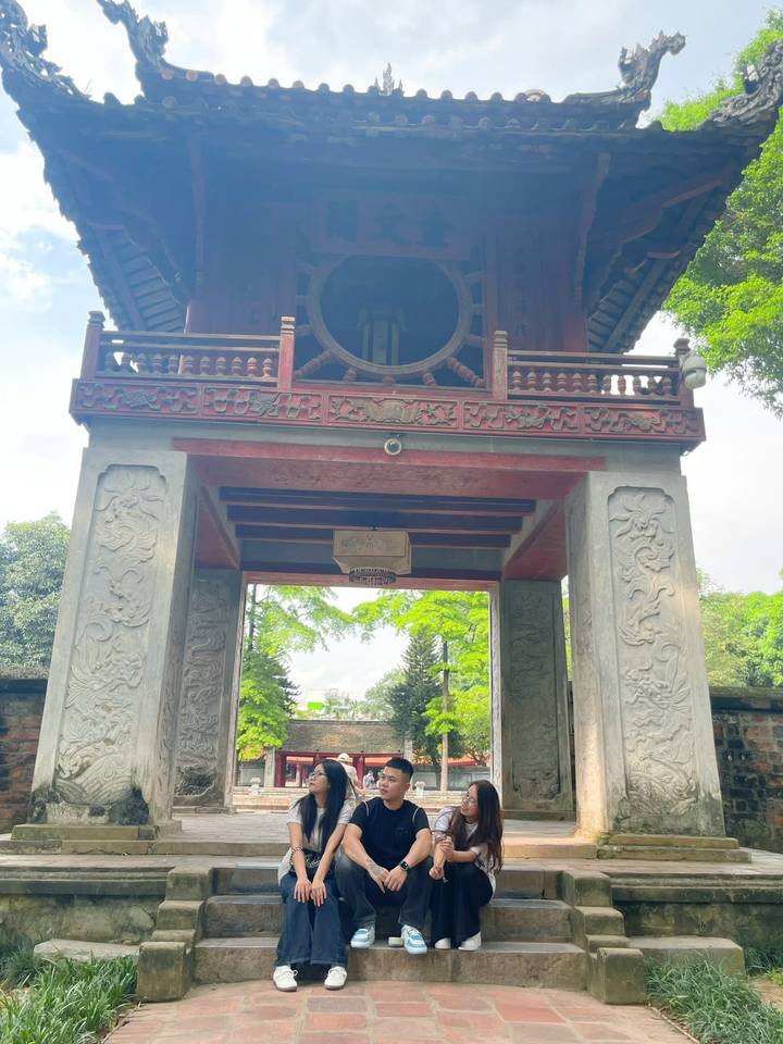 Stone gateway with carved pillars and a large bronze bell at Hanoi’s Temple of Literature.