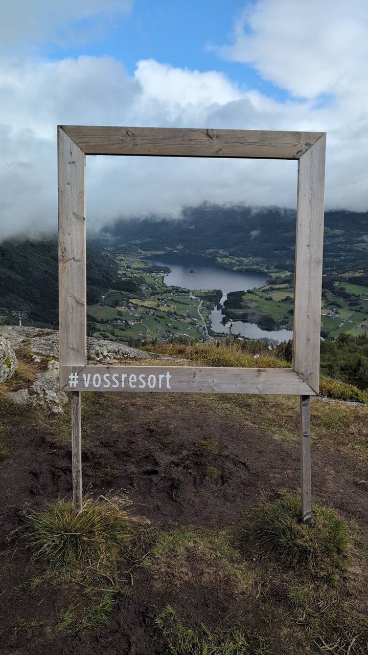 Wooden picture frame labeled #vossresort overlooks a verdant valley, lake, and villages below.