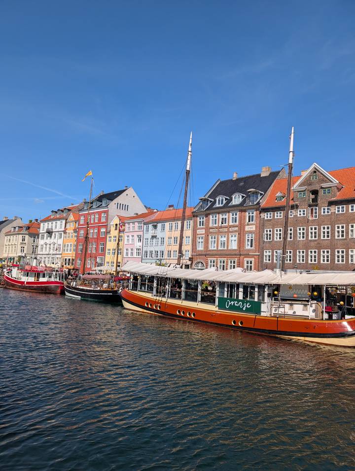 Colorful 17th-century canal houses line a busy waterfront with classic boats in bright sunshine.