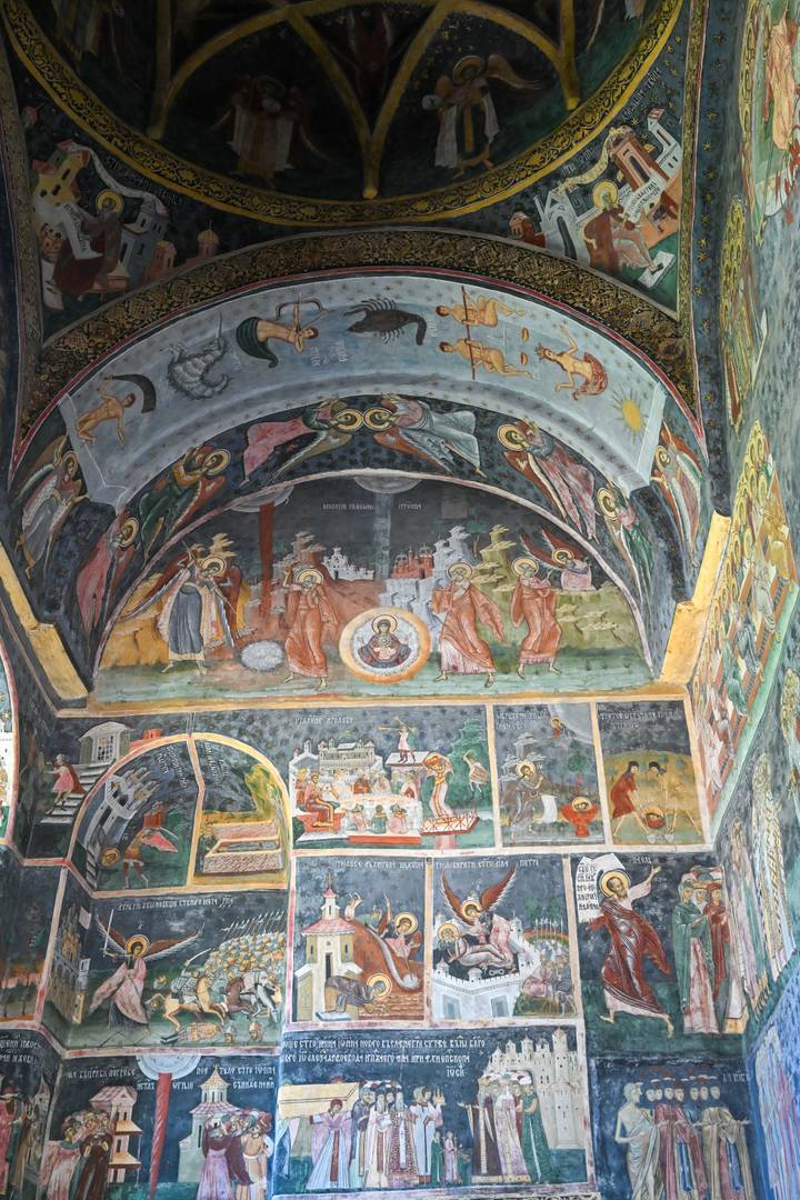Detailed interior frescoes of a Romanian painted monastery depicting vibrant biblical scenes.