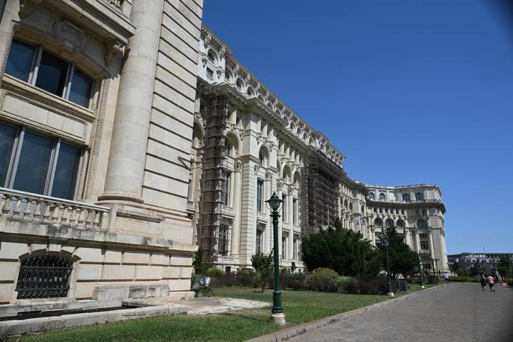 Side view of Romania's massive Palace of Parliament with ornate columns under a clear blue sky.